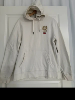 Morris Stockholm vit hoodie - Vit hoodie från Morris Stockholm med broderad logotyp på bröstet och en ficka på magen.  100% bomull. Nypris 1199kr 