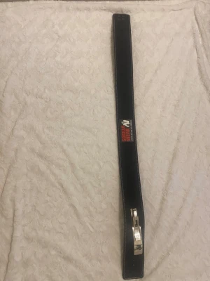 Svart träningsbälte Gorilla Wear - Säljer ett svart träningsbälte från Gorilla Wear med vit kontrastsöm och metallspänne. Bältet har en tydlig logga i rött och vitt framtill och är designat för att ge extra stöd vid styrketräning. Perfekt för dig som vill maxa på gymmet.