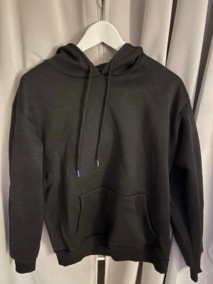 Svart hoodie med fjärilstryck - Svart hoodie med stor ficka framtill och dragsko i huvan. På ryggen finns ett vitt tryck av en fjäril som övergår i blommor från SHEIN i storlek M