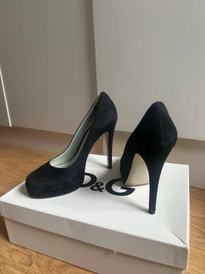 Svarta mockapumps från Dolce & Gabbana - Stilrena svarta pumps från Dolce & Gabbana i mjuk mocka. Skorna har hög klack och rundad tå, vilket ger en klassisk och elegant look. Perfekta för dig som vill ha en tidlös och lyxig sko med exklusiv känsla.