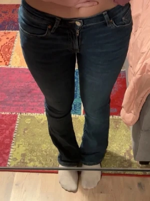 Blå bootcut jeans - Säljer ett par blå bootcut jeans med klassisk femficksdesign och låg midja. Jeansen har en lätt utsvängd passform nedtill och är tillverkade i ett stretchigt denimtyg som sitter snyggt på benen. Perfekta för en avslappnad och trendig look.