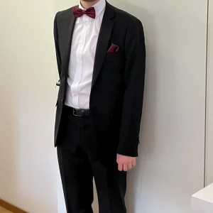 Svart kostym från Dressmann slim fit - Säljer en klassisk svart kostym från Dressmann i slim fit-modell. Kavajen har snygg passform och enkla knappar framtill. Byxorna är i storlek 32/32 och kavajen är storlek 48 regular. Perfekt för bal eller fest! Använd bara en gång- tvättad. 