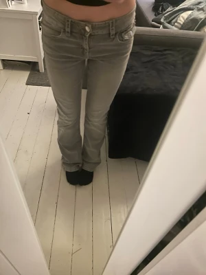 Grå bootcut jeans med detaljer i strl 164 - Säljer ett par grå bootcut jeans med snygga fickdetaljer bak och dekorativa knappar. Jeansen har låg midja och klassisk femficksmodell. Materialet är mjukt denim som sitter skönt och följsamt. Perfekta för dig som gillar en avslappnad men ändå trendig look.