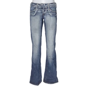 Blå bootcut jeans  - Snygga blå bootcut jeans med slitna detaljer och klassiska kontrastsömmar. Jeansen har låg midja, fem fickor och markerade sömmar framtill och baktill. Perfekta för en avslappnad och trendig look. Midjemåttet är 76 cm och innerbenslängden 84 cm