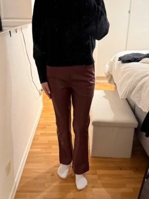 Vinröda bootcut jeans i skinnlook - Snygga vinröda jeans med bootcut-modell och skinnliknande material. Byxorna har hög midja och raka ben som slutar med lätt utsvängning. Perfekta för dig som vill ha en trendig och edgy stil.