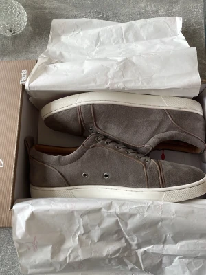 Loubs  - Snygga sneakers i grå mocka från Louboutin med röda sulor. Insidan är fodrad i beige läder för extra komfort. Fint skick, liten defekt på sista bilden! Skorna har använts till och från men skickade in de på rengöring och har inte använt de sen dess. Just nu är de för små för mig och därför säljer jag de för ett bra pris! Storlek 45 men skulle även säga att de passar 44. Kan frakta samma dag som köp görs😁