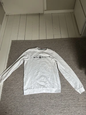 Vit långärmad tröja Sail Racing knappas använd. - Vit långärmad tröja från Sail Racing med svart logotyptryck på bröstet och en liten logga i nacken. Klassisk rund halsringning och ribbade muddar vid ärmslut och nederkant. Perfekt för en clean och sportig stil.