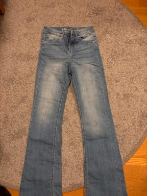 Ljusblå bootcut jeans från L.A.B. - Säljer ett par ljusblå bootcut jeans från L.A.B. Jeansen har klassisk femficksdesign, lätt slitna detaljer och utsvängda ben. Perfekta för dig som gillar en avslappnad och trendig look. Materialet är mjukt denim som sitter skönt hela dagen. Hög midja
