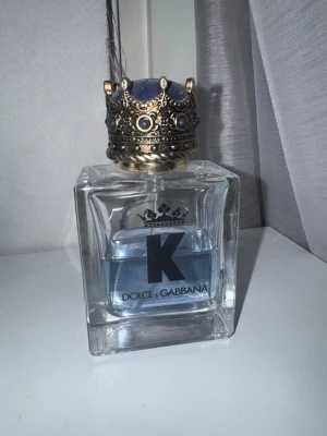 Dolce & Gabbana K Eau de Toilette - Dolce & Gabbana K Eau de Toilette i en stilren, fyrkantig glasflaska med blått innehåll och en unik kronformad kork i guld och blå detaljer. Medföljer lyxig blå och guld kartong. Perfekt för dig som vill ha en elegant och maskulin doft. Ca 30 av 60ml kvar