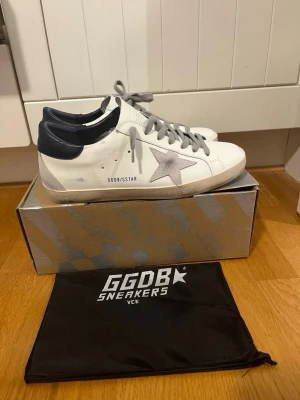 GGDB Superstar vita sneakers - Snygga vita GGDB Superstar sneakers med grå stjärna på sidan, grå skosnören och mörkblå häl. Klassisk låg modell i läder med slitna detaljer för en cool look. Perfekta för dig som gillar streetstyle och exklusiva märken. Pris kan diskuteras storlek 44
