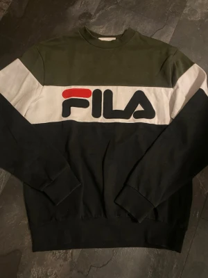 FILA sweatshirt i svart och olivgrön S - Snygg sweatshirt från FILA med breda blockfärger i svart, olivgrönt och vitt. Stor logga framtill i svart och rött. Tröjan har rund halsringning och ribbade muddar vid ärmslut och nederkant. Perfekt för en avslappnad streetwear-look.