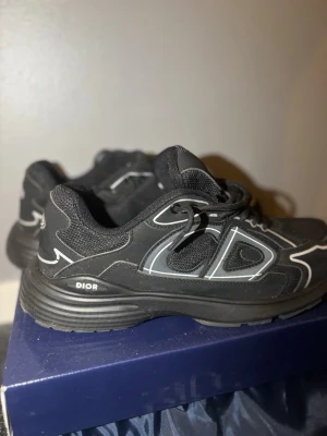Dior B30 - Snygga svarta Dior B30 sneakers med reflekterande detaljer och meshpaneler. Skorna har en sportig design med tydlig Dior-logga på sidan och plös, samt svarta snören och robust sula. Perfekta för dig som gillar exklusiva skor !  Frakt löses så snabbt som möjligt! ⭐️använda fåtal gånger, slitage finns inne på sulan, texten dior är sliten. Men inget som syns!⭐️Har du frågor eller funderingar så hör gärna av dig🤗 Dustbag samt box osv följs med vid köp⚡️skulle även säga att storleken är nog något liten.