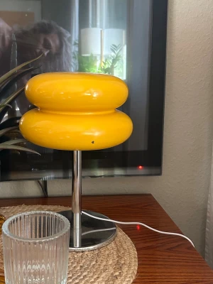 Retro gul bordslampa i metall och plast - Cool retro bordslampa med klargul lampskärm i plast och fot i kromad metall. Lampan har en rund, futuristisk form och passar perfekt som färgklick i rummet. Strömsladd i vitt. Perfekt för dig som gillar unik inredning.