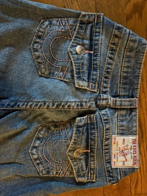 Blå True Religion jeans - Säljer ett par klassiska blå jeans från True Religion med ikoniska kontrastsömmar och snygga ficklock bak i Becca modellen. Midjemåttet är 31 cm och innerbenslängden är 68 cm. 