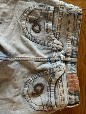 Ljusblå bootcut jeans från Gallop - Säljer ett par ljusblå bootcut jeans från Gallop med snygga broderade fickor och en stjärna. Jättesnygga! Midjemåttet är 35 cm och innerbenslängden är 75 cm . Jeansen lite upptrampade vid bensluten, se sista bilden.