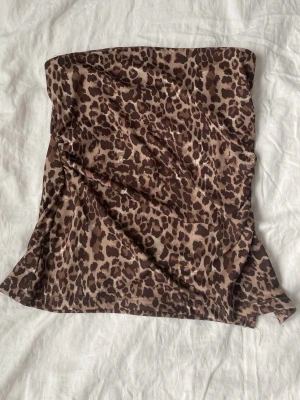 Leopardmönstrad tubtopp - Säljer en leopardmönstrad tubtopp i bruna och beige toner. Toppen är axelbandslös och har en tight passform som sitter snyggt på kroppen. Perfekt för dig som vill sticka ut med ett djurmönster. Materialet känns mjukt och följsamt.