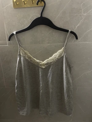 Grå linne med spetsdetalj - Mysigt grått linne med tunna axelband och vacker vit spets längs v-ringad hals. Perfekt för chill dagar hemma eller som loungewear. 