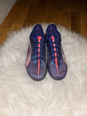 Blåa Puma fotbollsskor med röd detalj - Säljer ett par snygga fotbollsskor från Puma i mörkblått med röda och vita detaljer. Skorna har en smal siluett, snörning och ovandel i syntetmaterial som ger bra bollkontroll. Perfekta för dig som vill sticka ut på planen med stilrena och sportiga skor.Priset är inte fast det kan diskuteras 