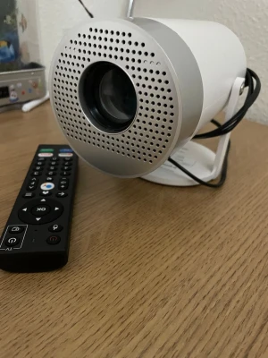 Vit mini-projektor med fjärrkontroll - Säljer en kompakt och stilren vit mini-projektor med rund form och perforerad front. Medföljer svart fjärrkontroll med många funktioner. 