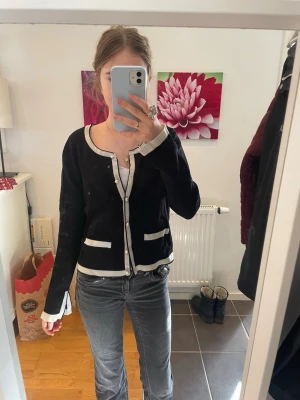 Svart kofta med vita detaljer - Säljer en svart kofta med vita detaljer som ger en old money look. Storleken är L men passar som S.