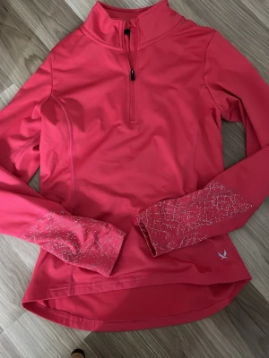 Rosa träningsöverdel med halv dragkedja - Snygg rosa långärmad träningsöverdel med halv dragkedja framtill och reflexdetaljer på ärmarna. Tillverkad i ett stretchigt funktionsmaterial som andas, perfekt för löpning eller gym. Liten logga på ena sidan nedtill.