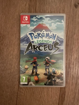 Pokémon Legends Arceus till Switch - Pokémon Legends Arceus till Nintendo Switch är ett äventyrsspel där du utforskar en öppen värld och fångar Pokémon i Hisui-regionen. Omslaget har färgstark grafik med berg och flera Pokémon-karaktärer. Spelet kommer i ett plastfodral med tryckt omslag.