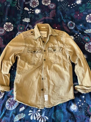  Abercombie & Fitch skjorta  - Grön-beige skjorta från Abercrombie & Fitch med sliten look med ett antal slitningar! Skriv vid minsta fundering !