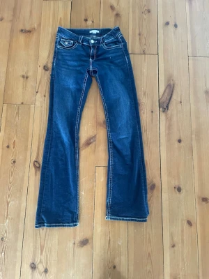 Mörkblå bootcut jeans från True Religion - Snygga mörkblå bootcut jeans med kontrastsömmar och klassiska fickdetaljer. Jeansen har låg midja och utsvängda ben, perfekt för en avslappnad och trendig look. Materialet är denim i bomull med en liten stretch.