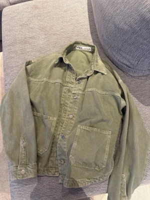 Olivgrön jeansjacka från Zara  - Säljer en olivgrön jeansjacka från Zara med avslappnad passform. Jackan har stora utanpåfickor, tryckknappar framtill och klassisk krage. Tillverkad i ett slitstarkt bomullstyg som ger en cool vintagekänsla. Perfekt att slänga över en hoodie eller t-shirt.