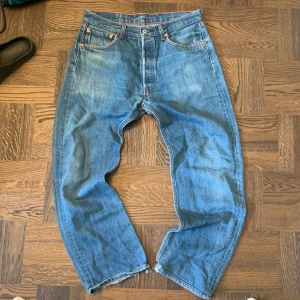 Levi's 501 blå jeans W34 L33 - Riktigt feta och klassiska Levi's 501 jeans i blå denim med raka ben och knappar i gylfen. Snyggt slitna detaljer och fransade benslut för en avslappnad vibe, precis som man vill ha dem. Perfekta för dig som gillar vintagekänsla och tidlös stil. Vet att det står L36 på baksida lappen men dem passar mer L33. Vid frågor och funderingar är det bara att fråga på! 