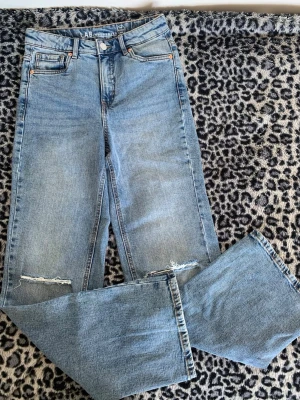 Blå jeans från LAB Industries - Säljer ett par ljusblå raka jeans från LAB Industries med slitna detaljer vid knäna. Jeansen har klassisk femficksdesign, hög midja och är tillverkade i mer hållbar denim. Perfekta för en avslappnad och trendig look.