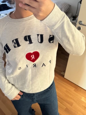 Vit långärmad topp från Superdry - Vit långärmad topp från Superdry med trycket 'SUPERDRY PARIS' och ett rött hjärta på bröstet. Lite knopprig text. Storlek L men liten och passar som M