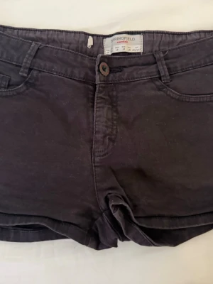 Svarta shorts från Springfield - Säljer ett par svarta shorts från Springfield med klassisk femficksdesign och knappgylf. De har bälteshällor och är tillverkade i mjuk bomull, perfekta för varma dagar. Passformen är normal och modellen är enkel och stilren.