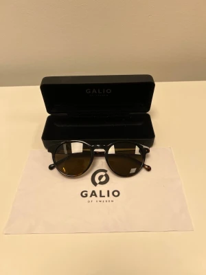 Gallo of Sweden solglasögon - stilrena, UV400, fodral ingår - Galio of Sweden solglasögon i stilren modell. Snygg mörk/sköldpaddsfärgad båge med tonade glas – lättmatchade och funkar till både vardag och sommarlooks. Skick: nya/ej använda 	•	Märke: Galio of Sweden 	•	UV400 	•	Kategori 3-linser 	•	Storlek: 50/22 145 	•	Fodral och putsduk ingår 	•	Skick: nya/ej använda (anpassa om du vill skriva “mycket fint skick” i stället)  Perfekta om du vill ha ett par snygga och prisvärda solglasögon.  Pris: 179kr Skickas gärna eller mötas upp