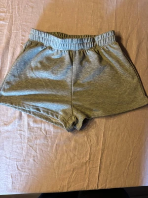 Grå mjuka shorts med resårmidja - Grå shorts i mjukt bomullsmaterial med elastisk midja. Klassisk och enkel design utan fickor eller detaljer, perfekta för chill dagar eller träning. Passformen är loose och de har en avslappnad look.