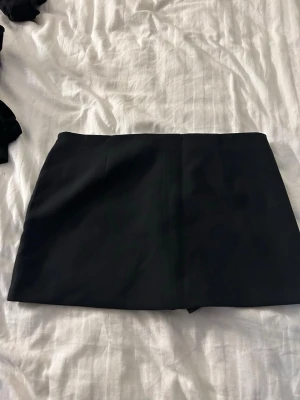 Svart kjol med inbyggda shorts med enkel design - Säljer en svart kjol med ingbyggdq shorts med stilren och minimalistisk look. Skorten har en rak passform och är sydd i ett mjukt, stretchigt tyg som ger en bekväm känsla. Perfekt för dig som gillar en clean och modern stil.