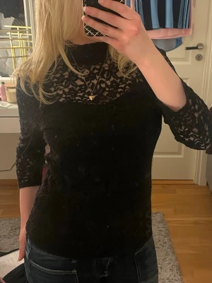 Svart spetsblus med trekvartsärm - Svart spetstopp med långa ärmar och transparent spets upptill. Stilren och elegant, passar både till vardag och fest. Säljer då den ej kommer till användning.