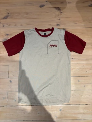 Beige och vinröd t-shirt från 100% - Snygg t-shirt från 100% med beige kropp och vinröda ärmar och krage. Tryck med '100%' på bröstet och markerad ficka. Tillverkad i ett lätt och ventilerande material, perfekt för en avslappnad stil.