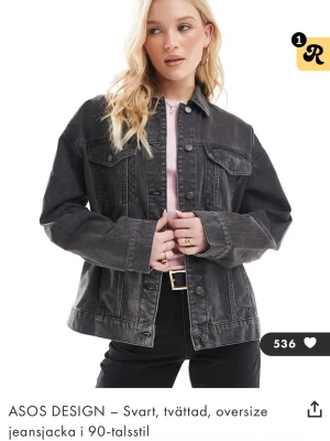 Svart oversize jeansjacka ASOS DESIGN - Snygg svart tvättad jeansjacka från ASOS DESIGN i oversize-modell med klassisk krage och knappstängning framtill. Jackan har två bröstfickor med lock och knappar samt markerade sömmar för en cool 90-talsvibe. 