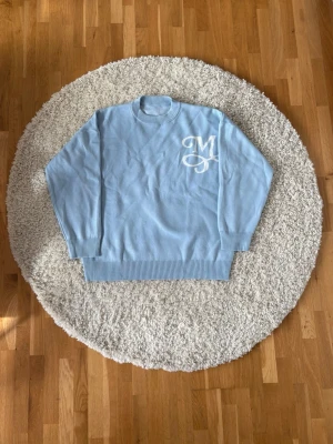 Ljusblå stickad Maison Monnaie tröja - Ljusblå stickad Maison Monnaie tröja med vita broderade bokstäver på bröstet och ryggen. Oversized passform och mjukt material. Pris kan diskuteras!