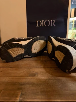 Dior b30 - Snygga svarta Dior sneakers med vita kontrastdetaljer och vita snören. Skorna har en chunky sula med CD-logga undertill och coola mönster längs sidorna. Perfekta för dig som vill ha en exklusiv och trendig look. Materialet är en mix av textil och syntet. Storlek 43 passar till 44. Pris kan diskutera. 