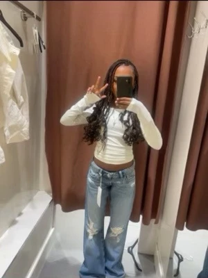 Blå slitna bootcut jeans - Säljer ett par ljusblå bootcut jeans med slitningar på båda knäna och råa kanter. Jeansen har låg midja och klassisk femficksdesign. Perfekta för en avslappnad och trendig look.