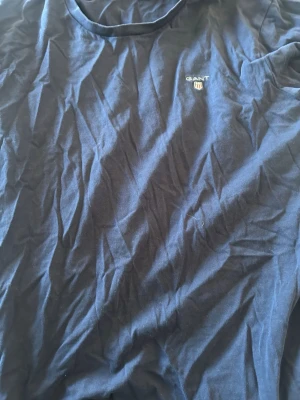 Marinblå t-shirt från GANT - Klassisk marinblå t-shirt från GANT med rund halsringning och broderad logga på bröstet. Tillverkad i mjuk bomull som känns skön mot huden. Perfekt basplagg för en clean och enkel stil.