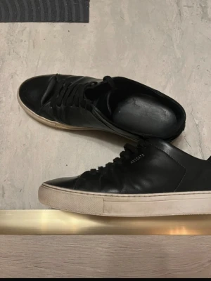 Svarta sneakers från Axel Arigato - Stilrena svarta sneakers från Axel Arigato i läder med vit sula och diskret logga på sidan. Klassisk låg modell med svarta skosnören och minimalistisk design som passar till det mesta.