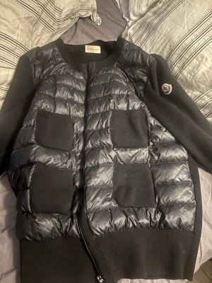 Moncler cardigan(kvitto finns) - Moncler cardigan i färgen svart, iprincip i nyskick ända defekten är att moncler loggan/lappen i nacken har lossat på ena sidan, men de går självklart att sy på igen och de är inget som syns när man har på sig den då de sitter på insidan. Har äkthetsbevis i form av orginalkvitto och prislapp❤️   Kommer bara sälja till ett bra pris då denna är i väldigt fint skick samt väldigt efterfrågad.
