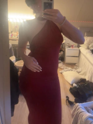 Vinröd oneshoulder långklänning - Säljer en vinröd långklänning med oneshoulder-design. Klänningen har en tight passform och är ärmlös, vilket ger en elegant och modern look. Perfekt för dig som vill sticka ut med en stilren och trendig outfit.