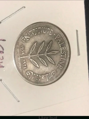 Palestina 100 mils mynt 1934 / 1 styck  - Säljer ett silverfärgat 100 mils mynt från Palestina, år 1934. Myntet har en olivkvist på ena sidan och text på engelska, arabiska och hebreiska. Perfekt för dig som samlar på historiska mynt eller gillar unika samlarobjekt.