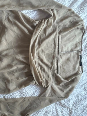 Beige långärmad blus från BikBok - Stilren beige blus från BikBok i storlek M. Blusen har långa ärmar och en snygg draperad detalj framtill. Tillverkad i ett tunt, lätt material som ger en luftig känsla. Perfekt att matcha med både jeans och kjol för en trendig look. Aldrig blivit använd 