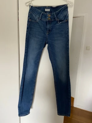 Blå high waist jeans från LINDEX - Snygga blå high waist jeans från LINDEX med raka ben och klassisk femficksmodell. Jeansen har dubbla knappar i midjan och är tillverkade i stretchigt denimtyg. 