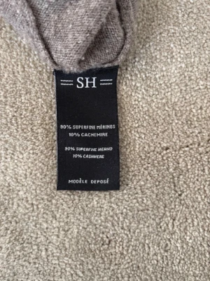 Beige hoodie i merinoull och cashmere - Mjuk och stilren beige hoodie från SH, tillverkad i 90% superfine merinoull och 10% cashmere. Hoodien har långa ärmar, ribbade muddar och en klassisk huva. Perfekt för dig som gillar en clean och lyxig look med premiumkänsla.